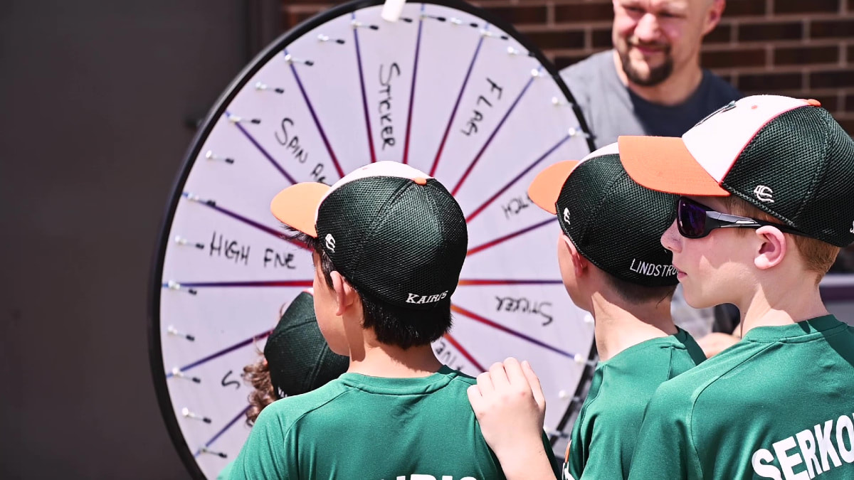 baseball players in green jerseys line up to spin prize wheel